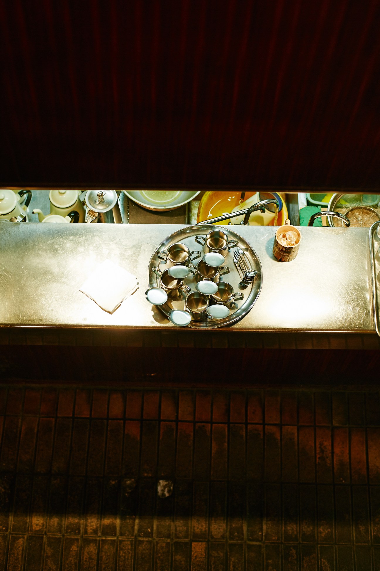 Overhead view of Coffee Lawn counter with brass coffee cups arranged on a tray and kitchenware visible above.