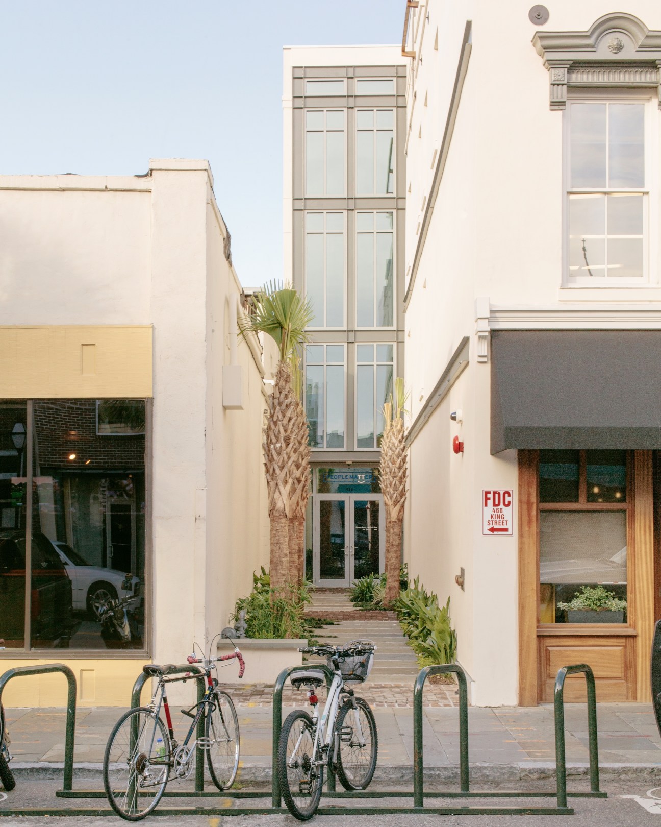 Bicycles parked in front of a narrow Charleston building with palmetto trees and large windows.