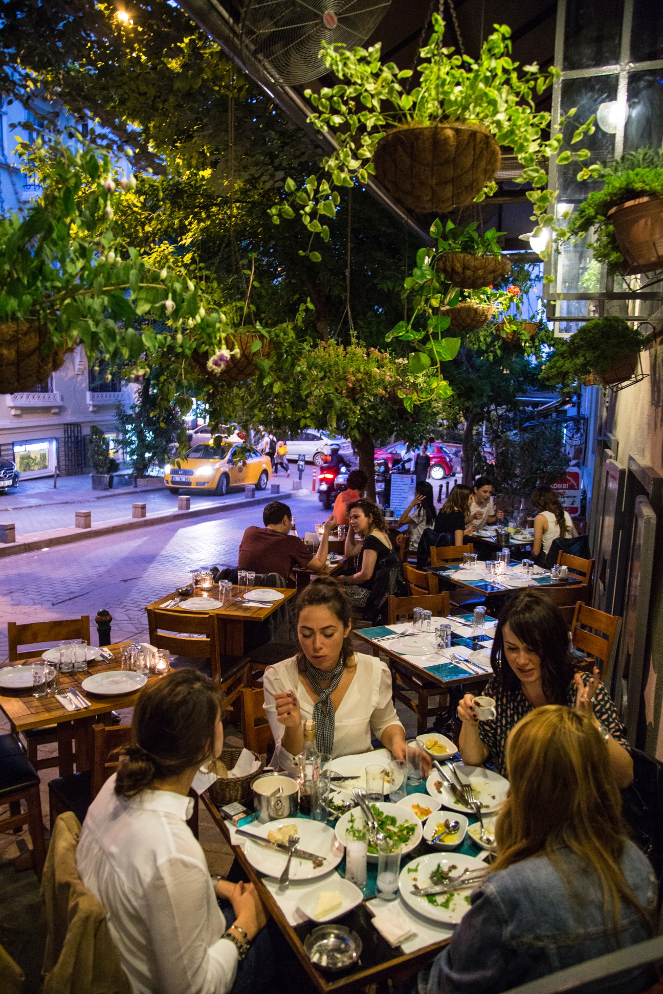 Diners enjoy meze and drinks at candlelit outdoor tables on Akarsu Caddesi in Istanbul at night.