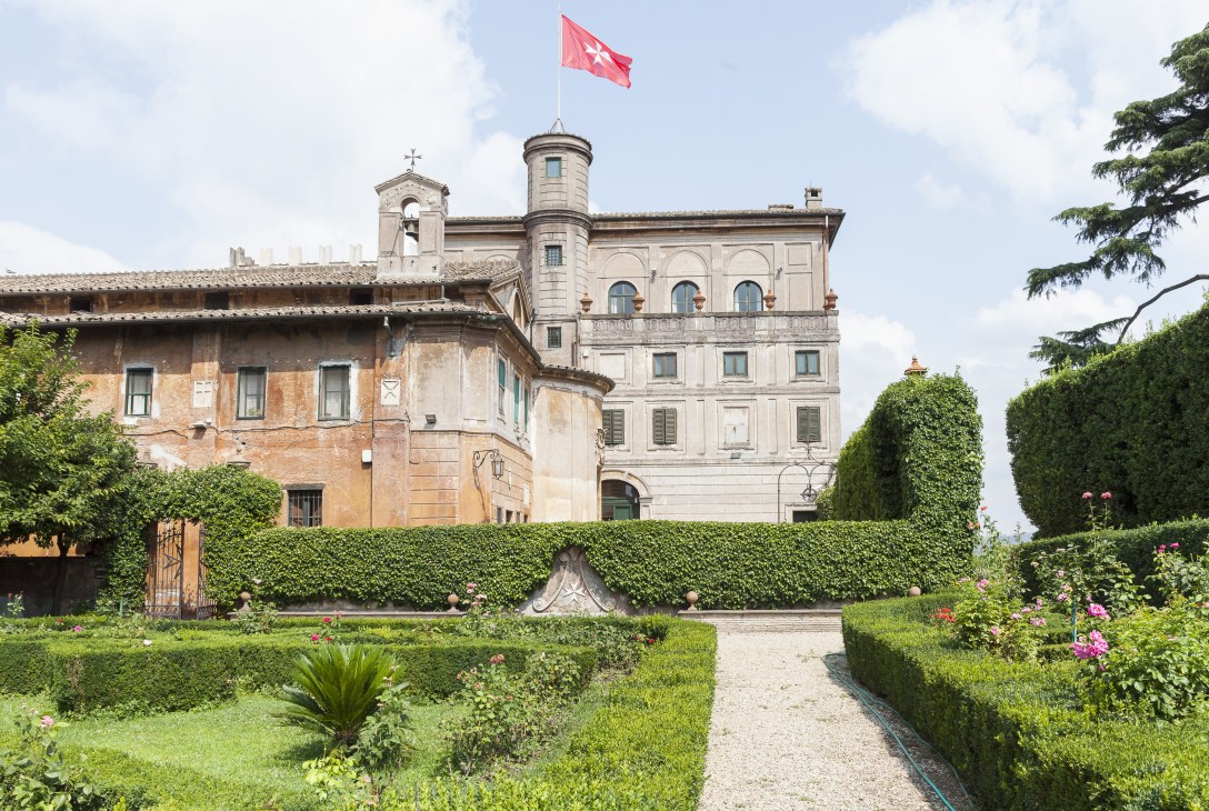 Villa Magistrale in Rome with manicured gardens, baroque architecture, and red flag flying above the tower.