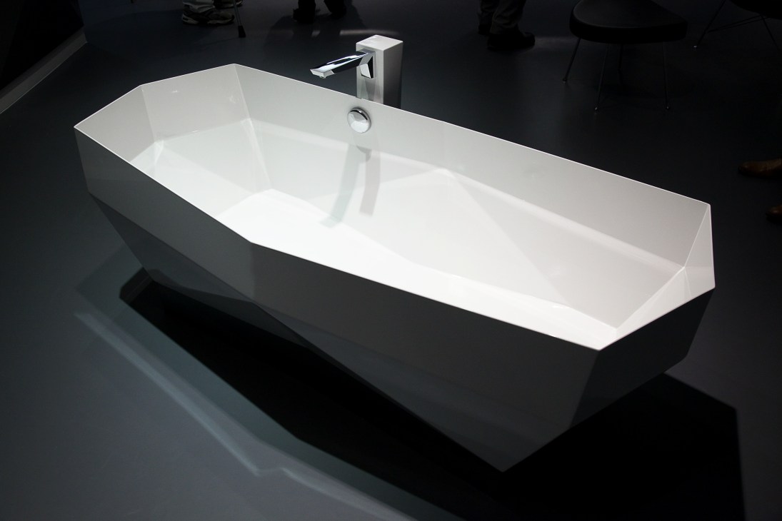 Modern white rectangular bathtub with minimalist chrome faucet and overflow drain against dark floor.