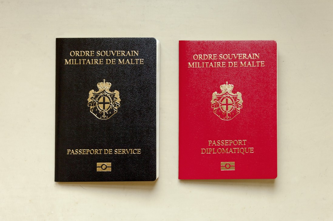 Two official passports of the Sovereign Military Order of Malta: a black service passport and a red diplomatic passport with gold embossing.
