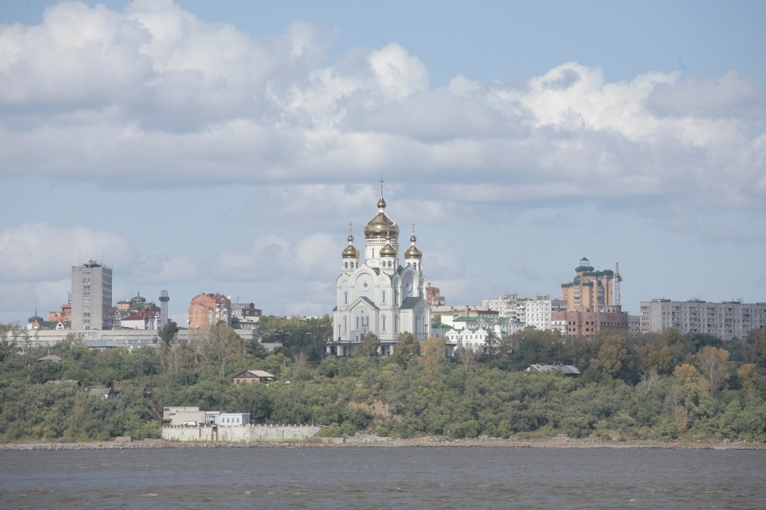 Khabarovsk skyline with white Orthodox church with golden domes overlooking the Amur River and Soviet-era apartment buildings.