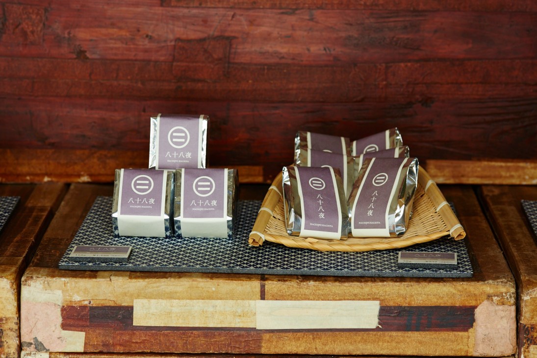 Packaged Maruni tea boxes with Japanese characters displayed on a woven tray against a wooden backdrop.