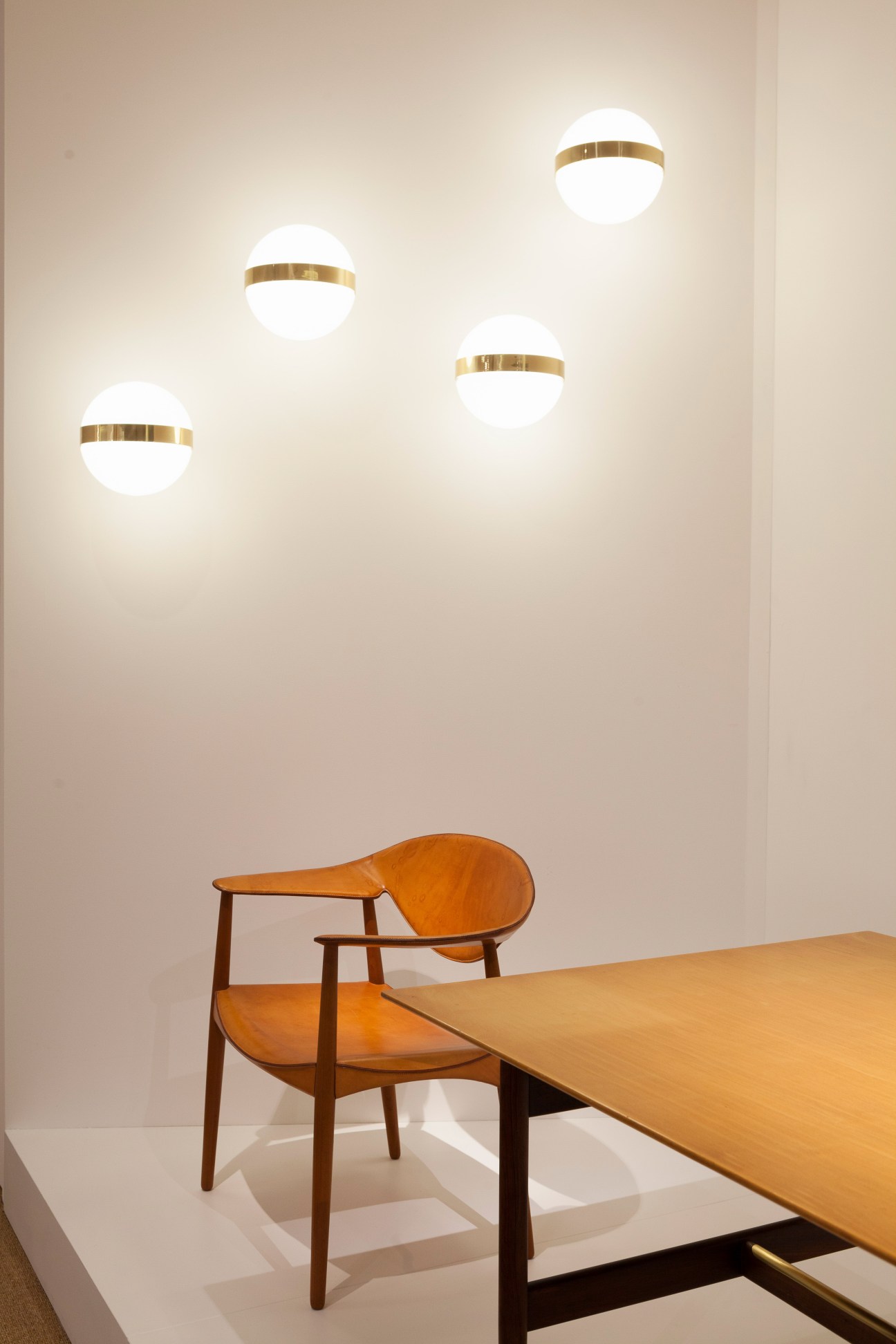 Mid-century wooden chair with orange seat and four glowing spherical ceiling lights with brass bands.