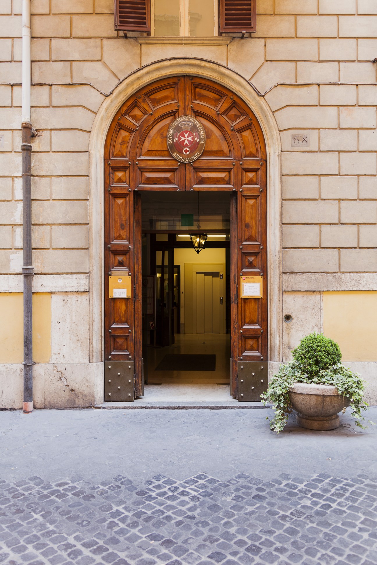 Ornate wooden arched entrance door to the Palazzo Magistrale with stone facade and ivy-covered planter.