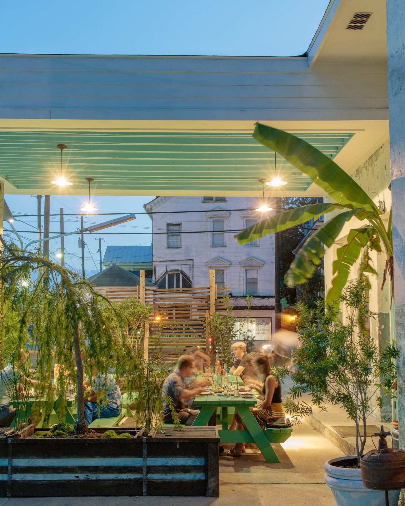 Diners seated at green picnic tables in an evening courtyard with plants and overhead lighting at Xiao Bao Biscuit restaurant.