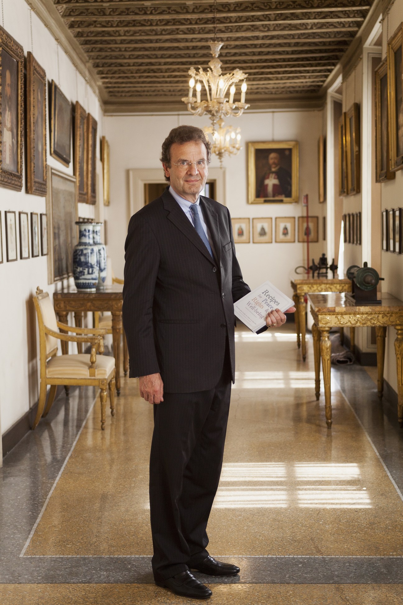 Grand chancellor HE Albrecht Freiherr von Boeselager stands in an ornate palazzo corridor holding a document.