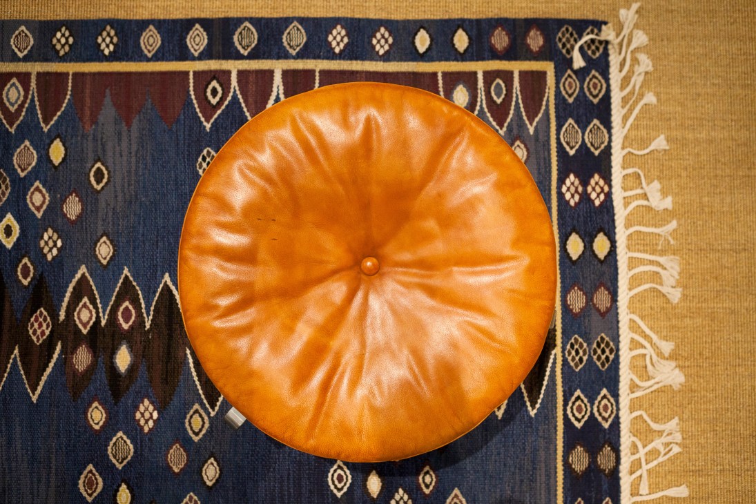 Orange leather Poul Kjaerholm PK33 stool displayed on a patterned blue and gold fabric rug.
