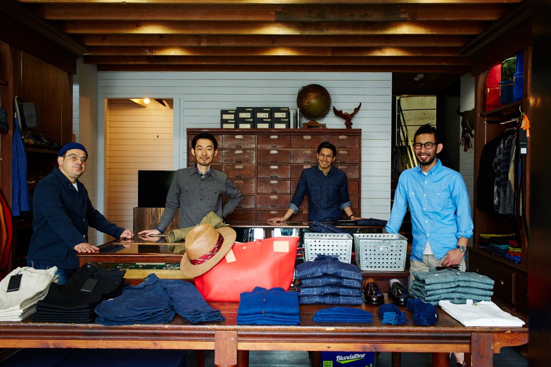 Four men stand behind a wooden counter displaying clothing and accessories in Freemans Sporting Club Tokyo store.