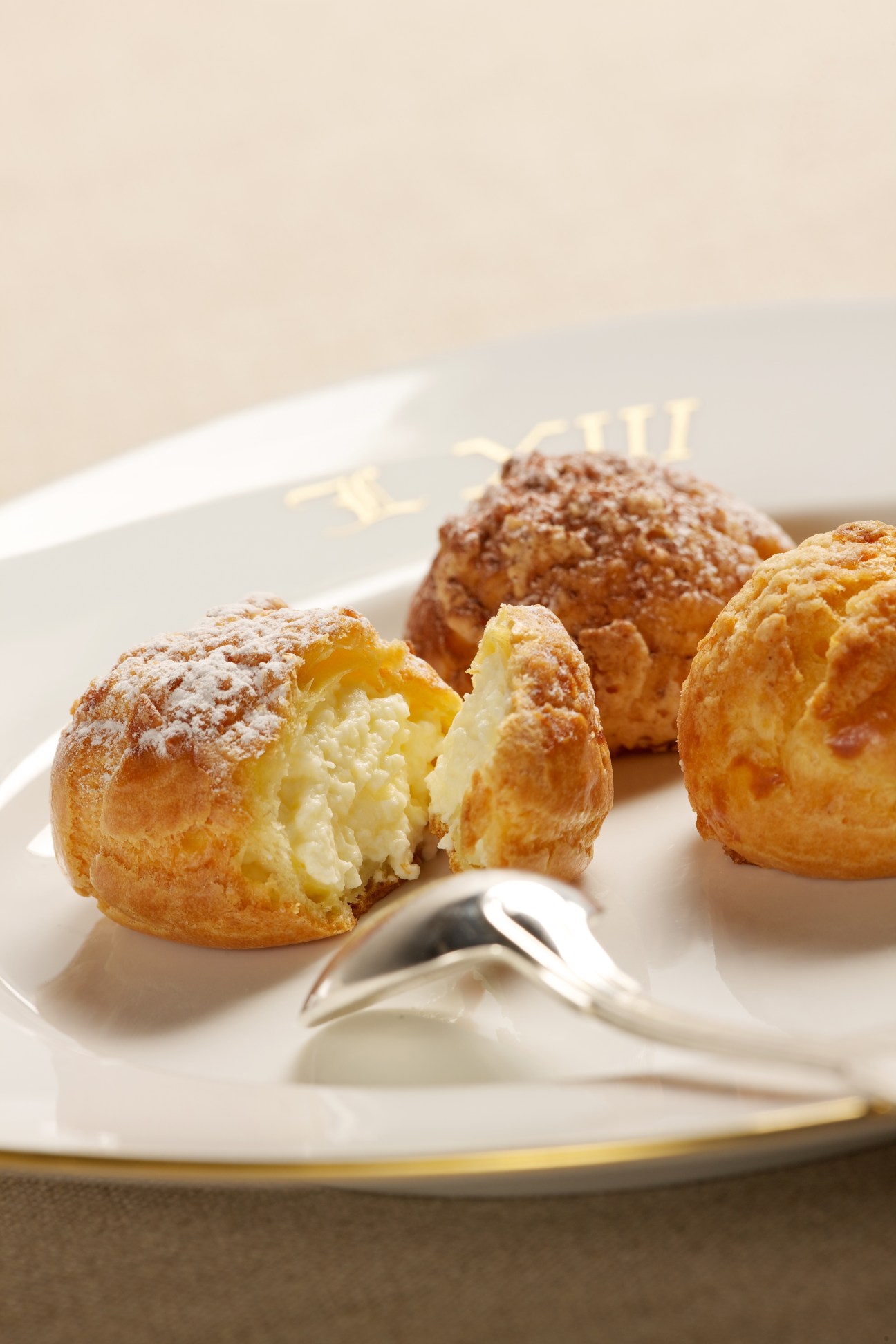 Cream-filled choux pastries dusted with powdered sugar on a white plate with a small spoon.