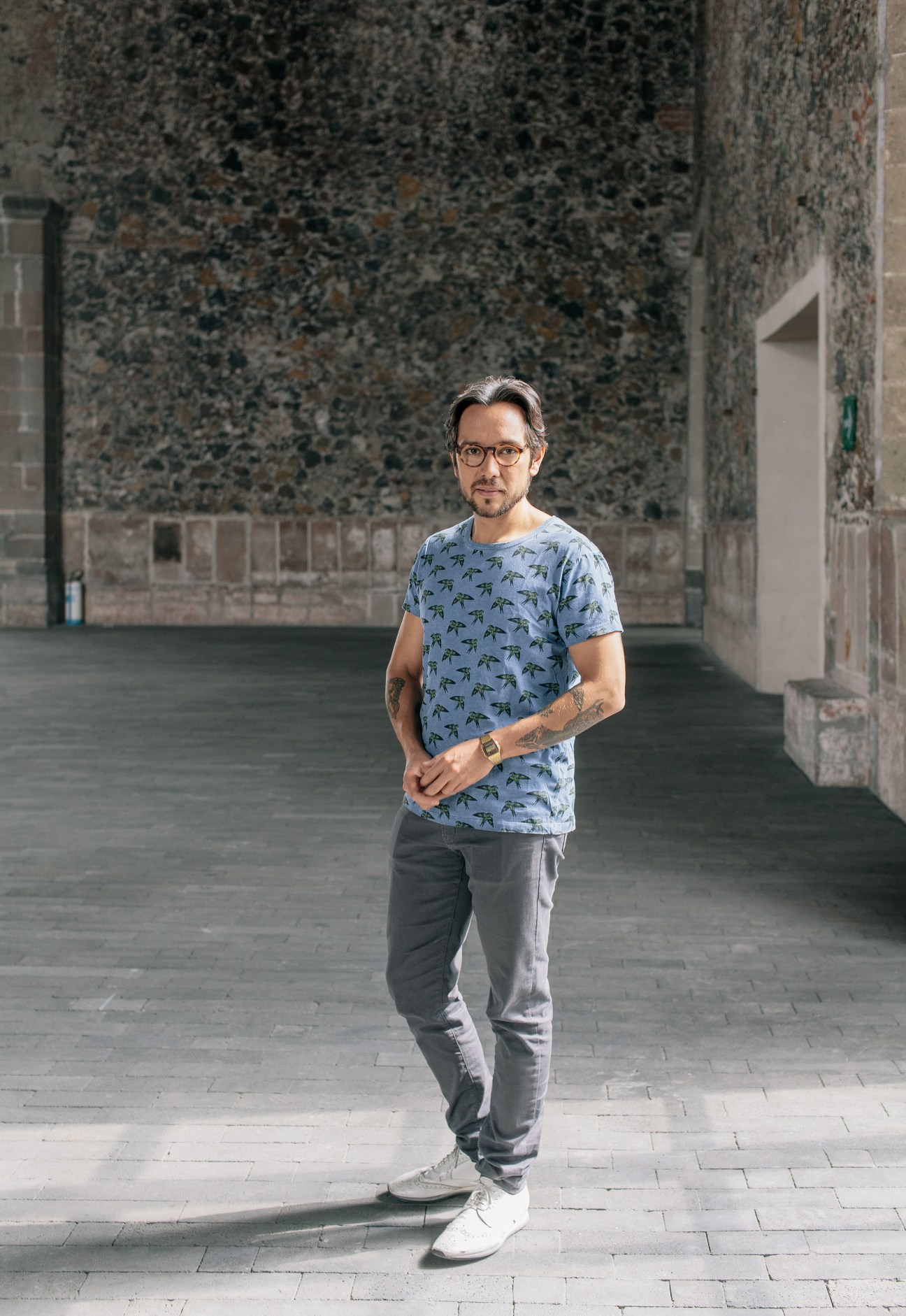 Political scientist Genaro Lozano standing in a courtyard wearing glasses and a patterned blue shirt.