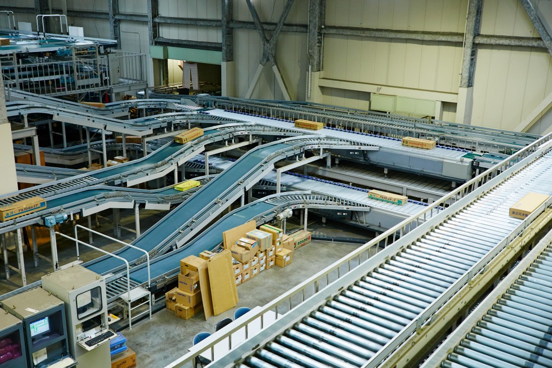High-speed conveyor belt system with multiple teal and silver tracks moving flower boxes through an industrial warehouse facility.