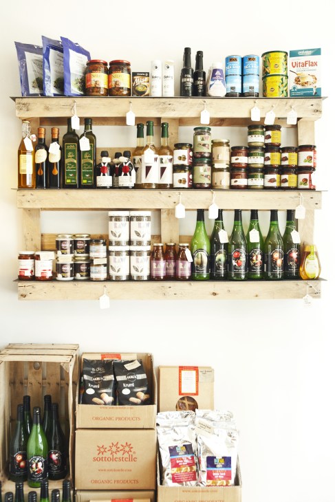 Wooden shelves displaying organic products including wines, oils, preserves, and packaged goods with white price tags at G&T in London.