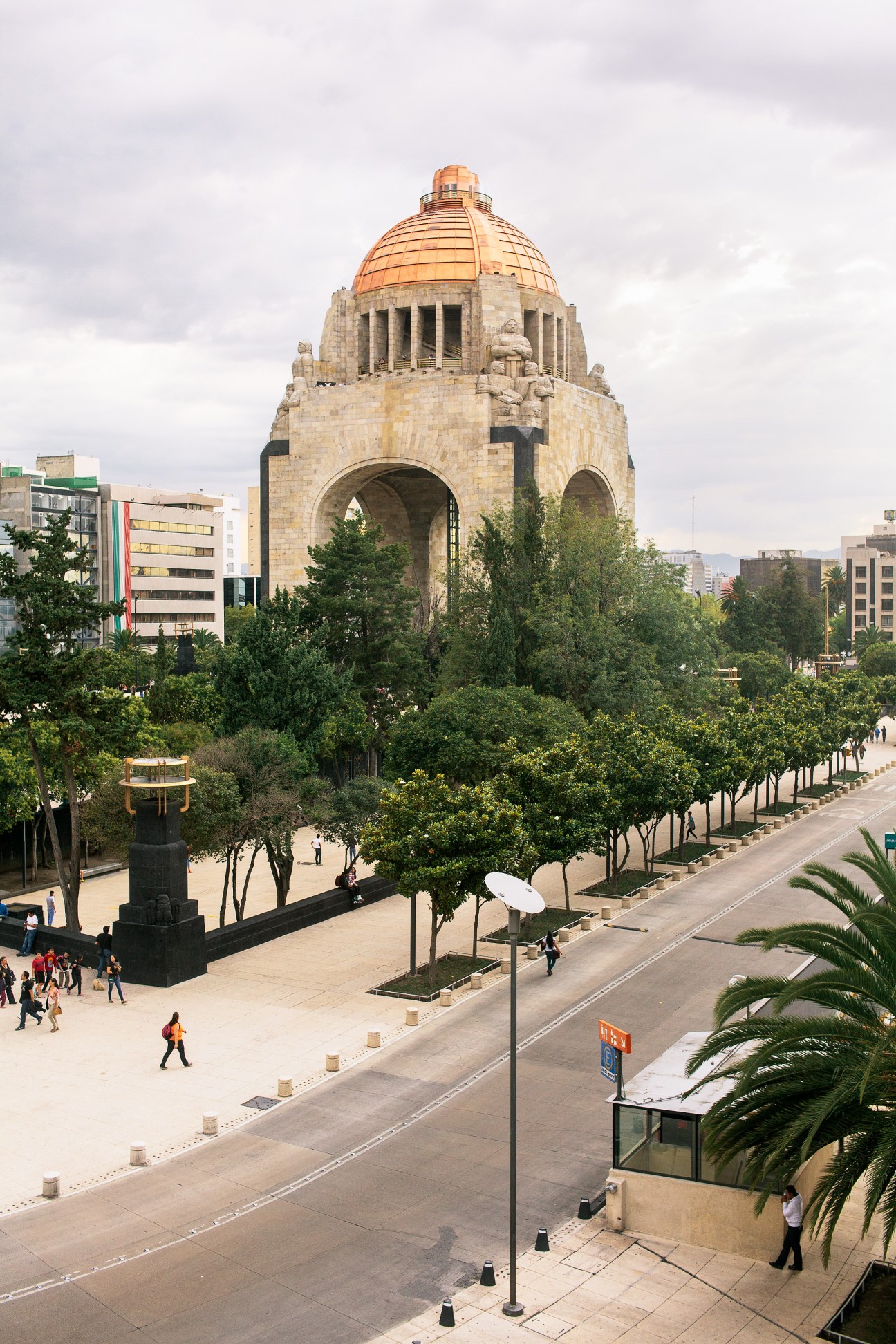 Monument to the Revolution with copper dome and stone columns surrounded by trees on Plaza de la República in Mexico City.
