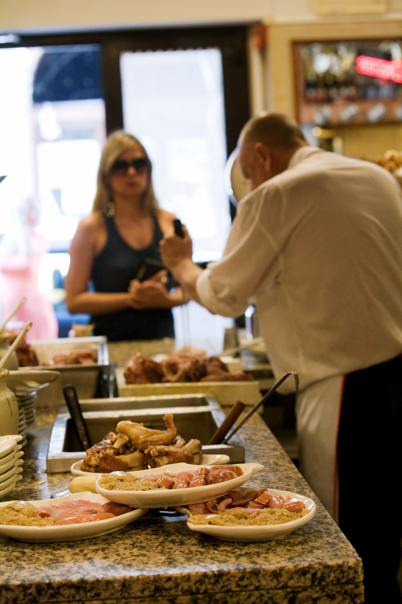 Customers at a counter in Da Pepi restaurant with plates of Italian food and charcuterie.