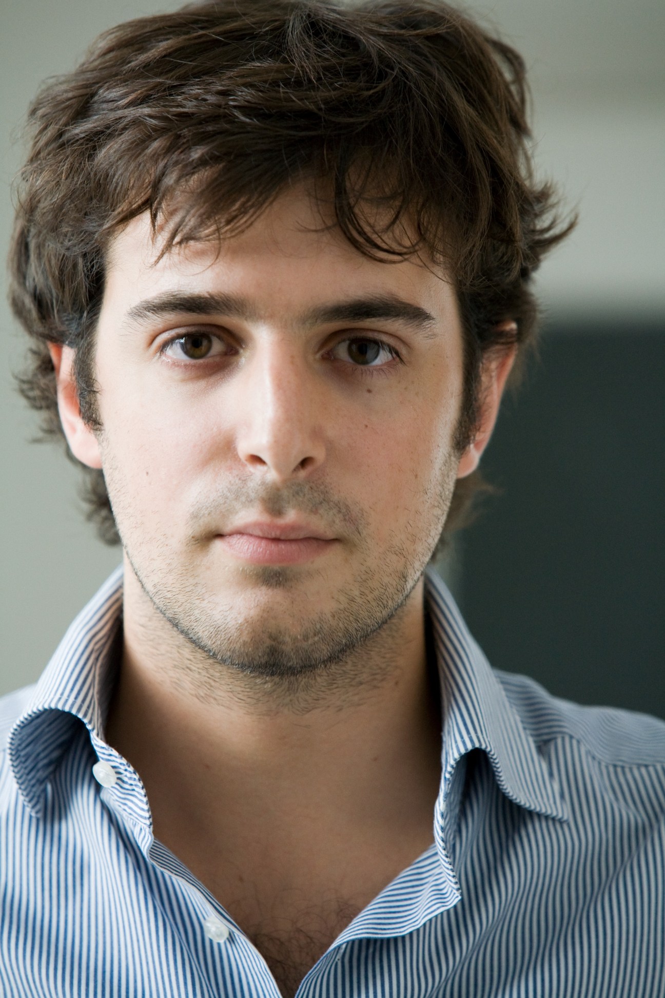 Portrait of Beniamino Pagliaro, a man with dark hair wearing a blue striped shirt.