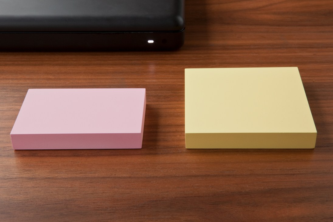 Two colorful Post-It note-inspired boxes, one pink and one yellow, displayed on a wooden surface next to a laptop.