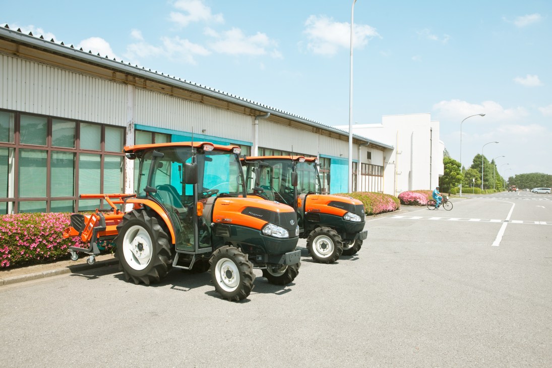 Orange and black Kubota tractors parked outside an industrial building with turquoise doors.