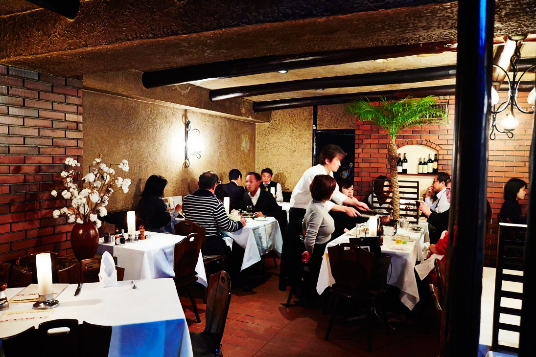 Interior of Chaco Amemiya steakhouse dining room with brick walls, wooden beams, and diners at tables.