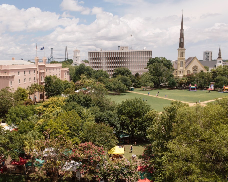 Marion Square in Charleston with green lawn, flowering trees, historic buildings and churches visible in cityscape.