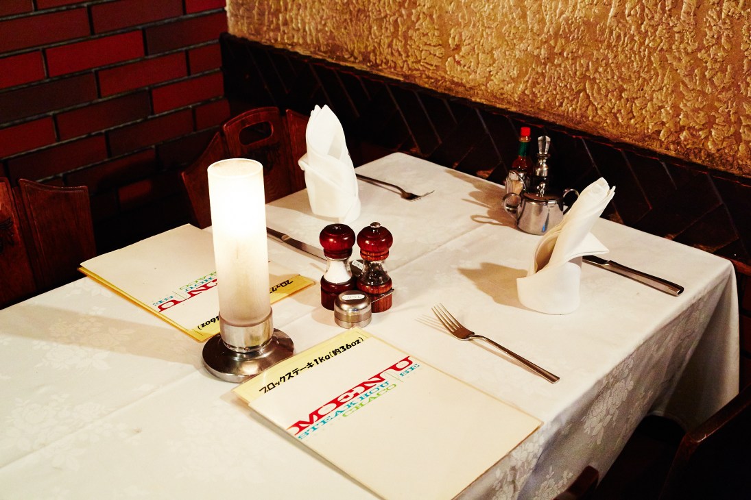 Yuichiro Miura's regular table at Chaco Amemiya restaurant, set with white linens, candle, salt and pepper shakers, and Japanese menu cards.