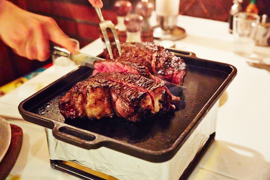 Rare rib-eye and fillet steaks sliced on a heated metal plate at a Tokyo steakhouse.
