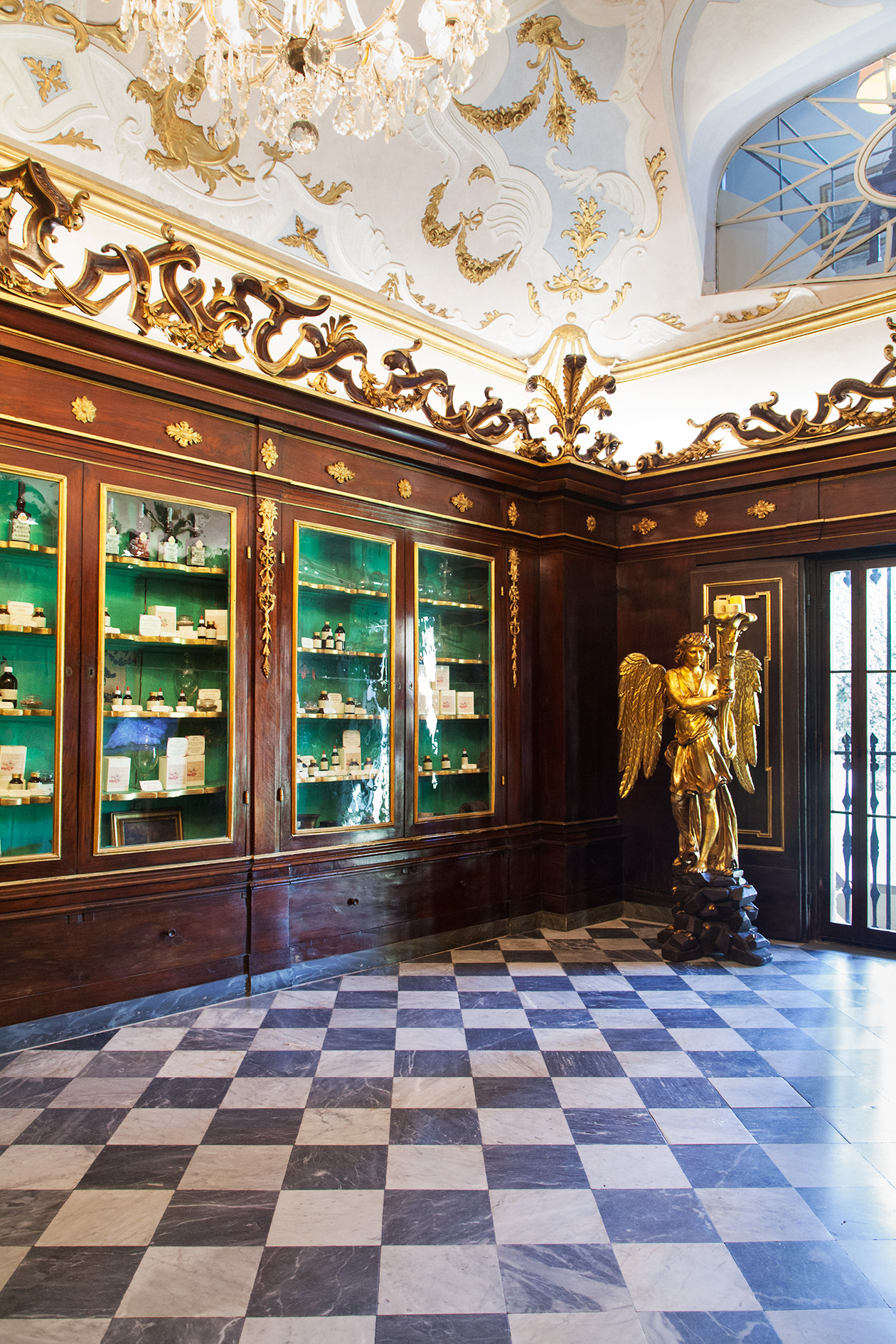 Ornate apothecary interior with green-backed display cabinets, gilded moldings, and marble checkerboard floor at Officina di Santa Maria Novella, Florence.