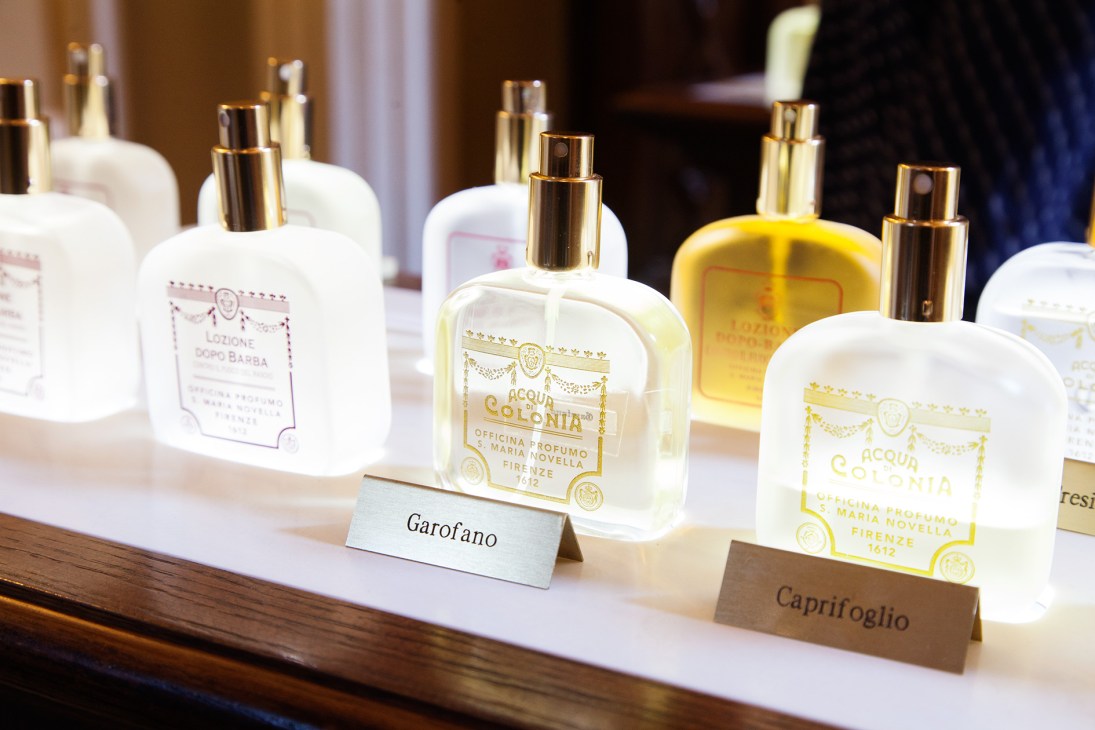 Display of Officina di Santa Maria Novella fragrances with gold-labeled bottles on white shelf.