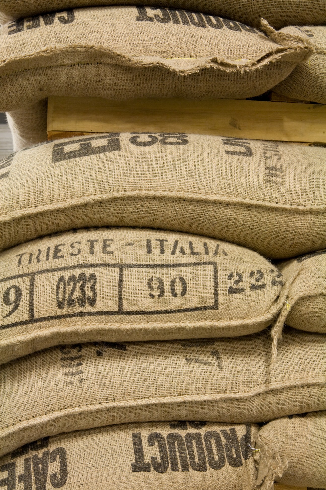 Stacked burlap sacks of arabica coffee beans labeled with origin information at Illy's Trieste warehouse.