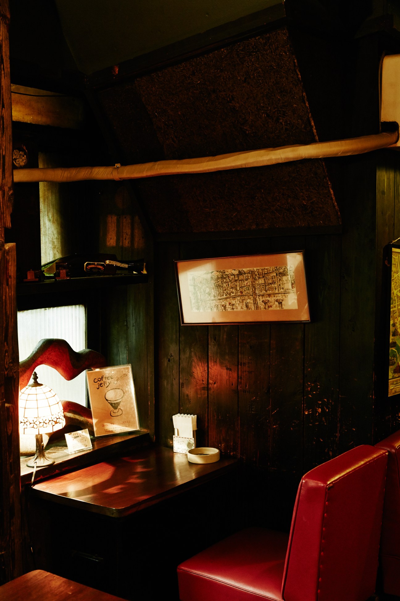 Interior of a vintage Tokyo kissaten café with dark wood, red seating, warm lighting, and vintage coffee memorabilia on display shelves.