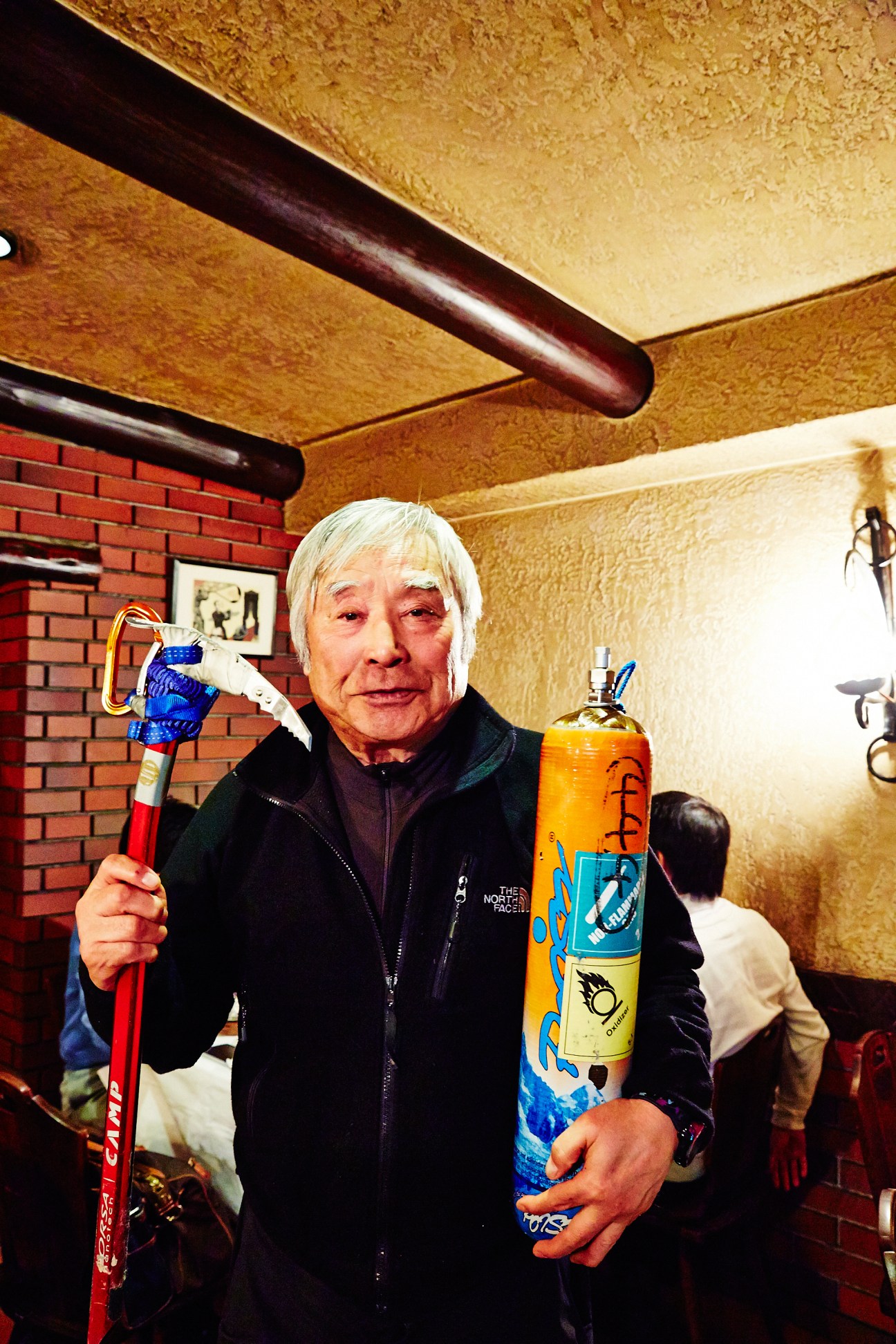 Yuichiro Miura holds an ice axe and oxygen tank used for mountain climbing.