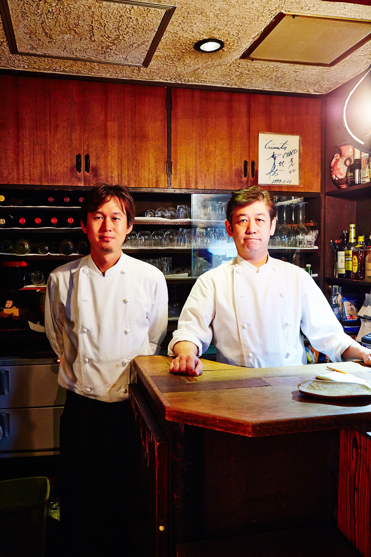 Two chefs in white chef's coats stand at the counter of Chaco Amemiya restaurant.