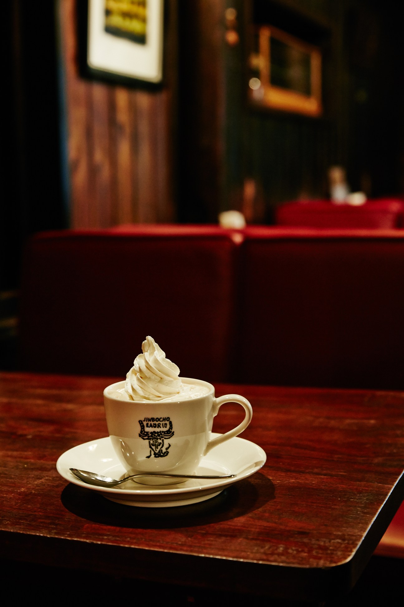 A cup of Vienna coffee topped with whipped cream sits on a wooden table in a dimly lit Tokyo café interior.