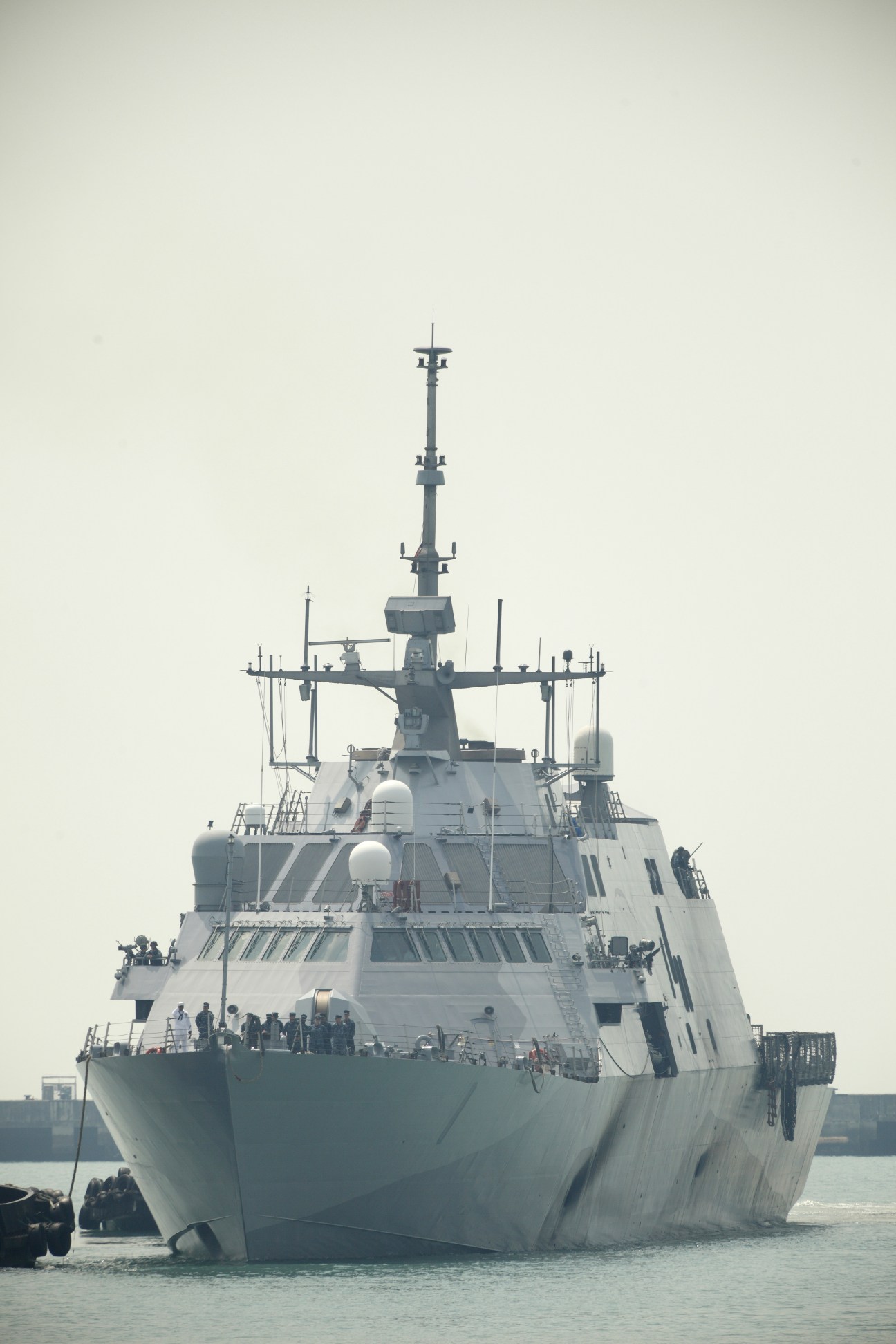 USS Freedom Littoral Combat Ship viewed from the front, showing its sleek white hull and tall mast in shallow coastal waters.