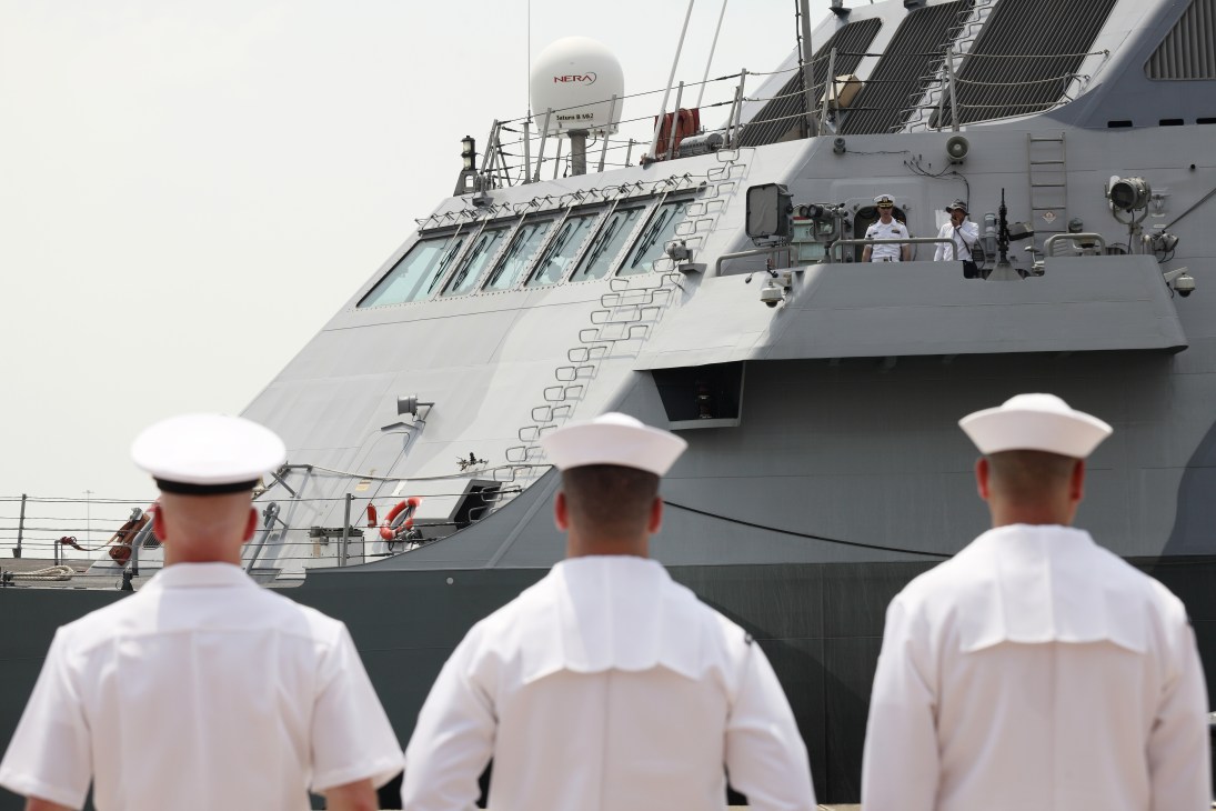 US Navy sailors in white uniforms greet the USS Freedom Littoral Combat Ship docking in Singapore.