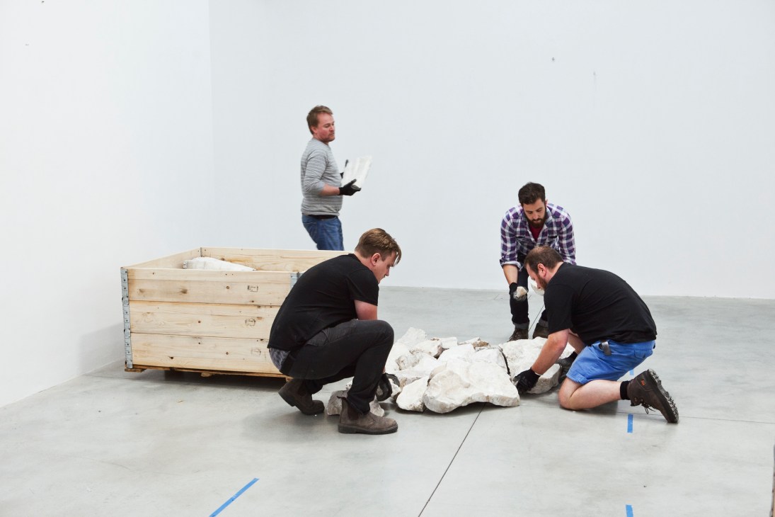 Technicians install Richard Long's 'White Onyx Line' artwork, arranging white stones on a gallery floor next to a wooden crate.