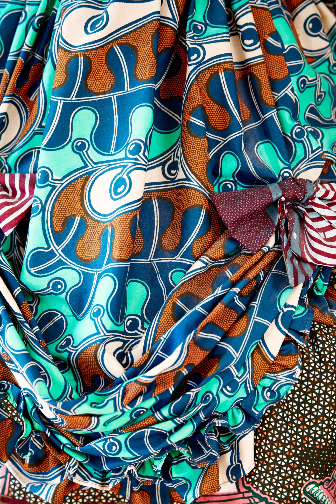 Vibrant batik fabric with blue, orange, and turquoise geometric patterns folded with contrasting striped textiles.