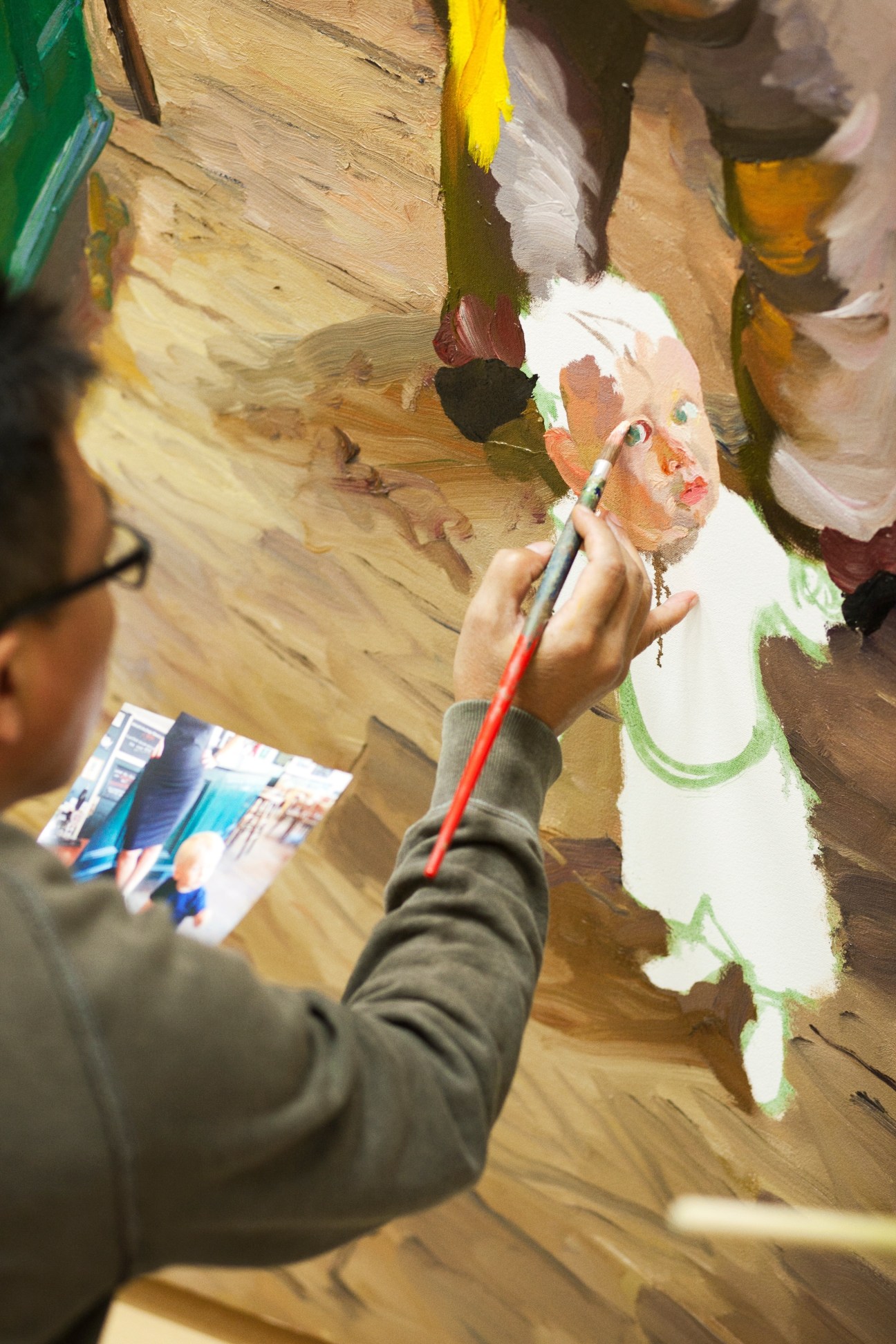 Artist Liu Xiaodong painting with a brush, working on a canvas with yellow, white, and green strokes.
