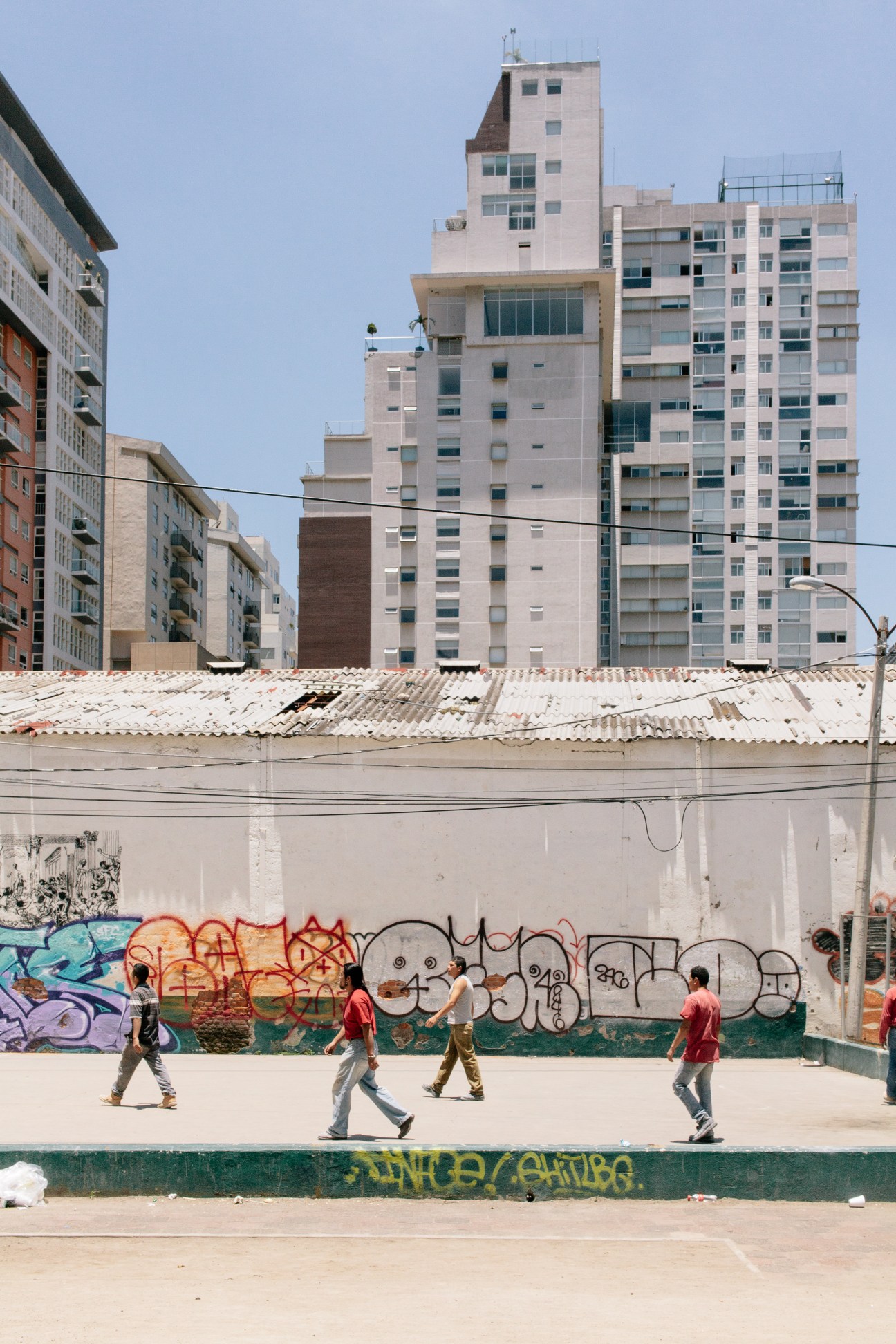 Young people playing football in an urban court surrounded by apartment buildings and graffiti-covered walls.