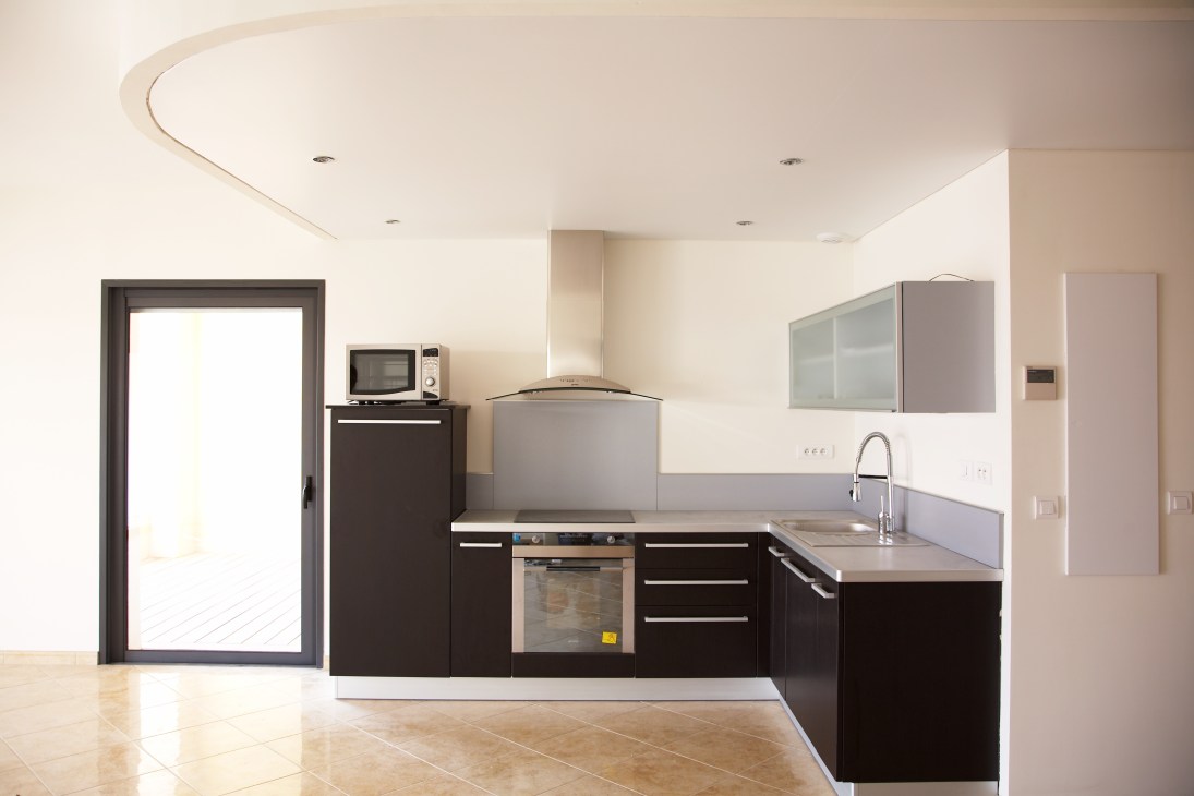 Modern apartment kitchen with black cabinetry, stainless steel appliances and light stone flooring in Calvi.