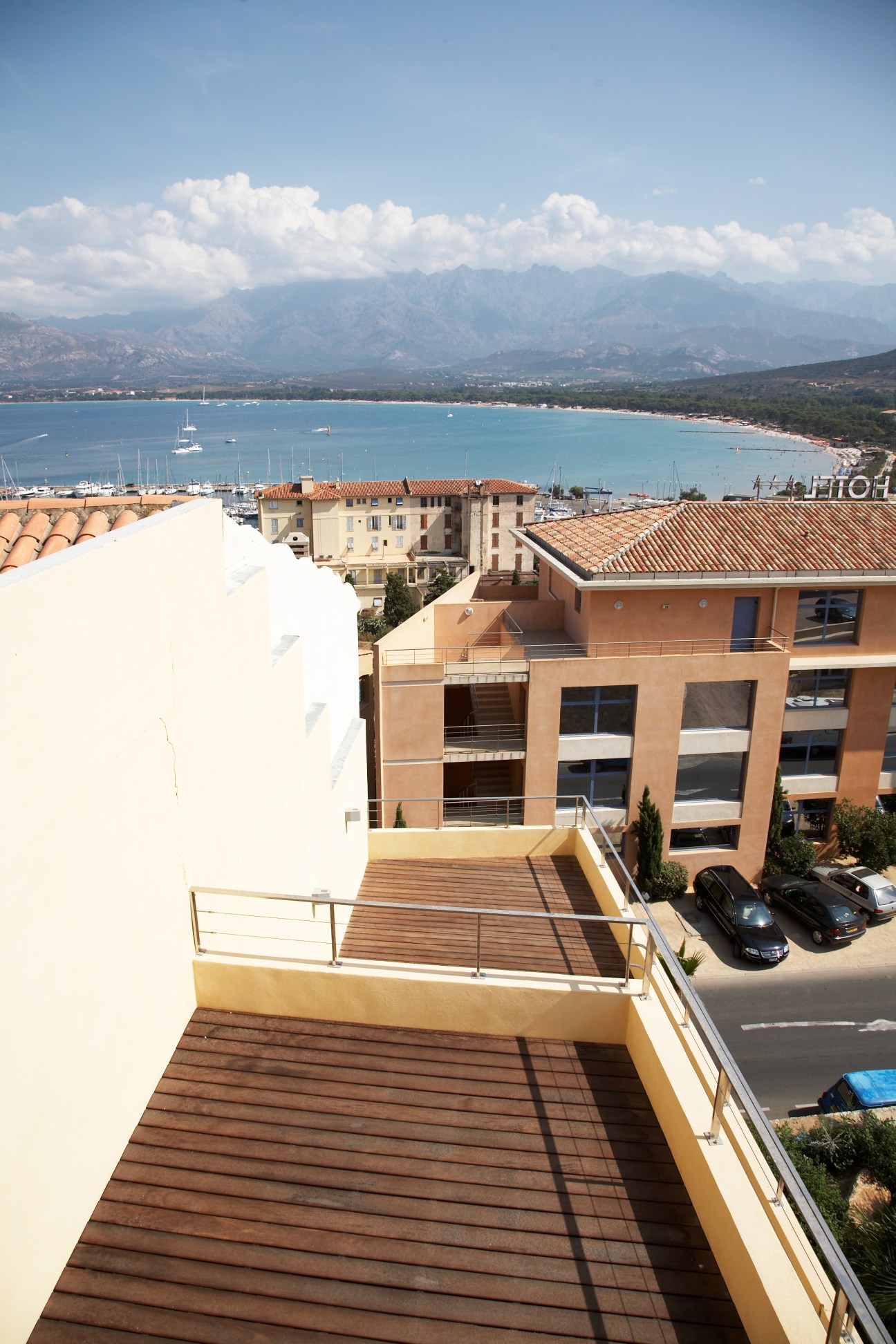 Roof terrace with wooden deck overlooking Calvi's turquoise bay, marina, and mountains.