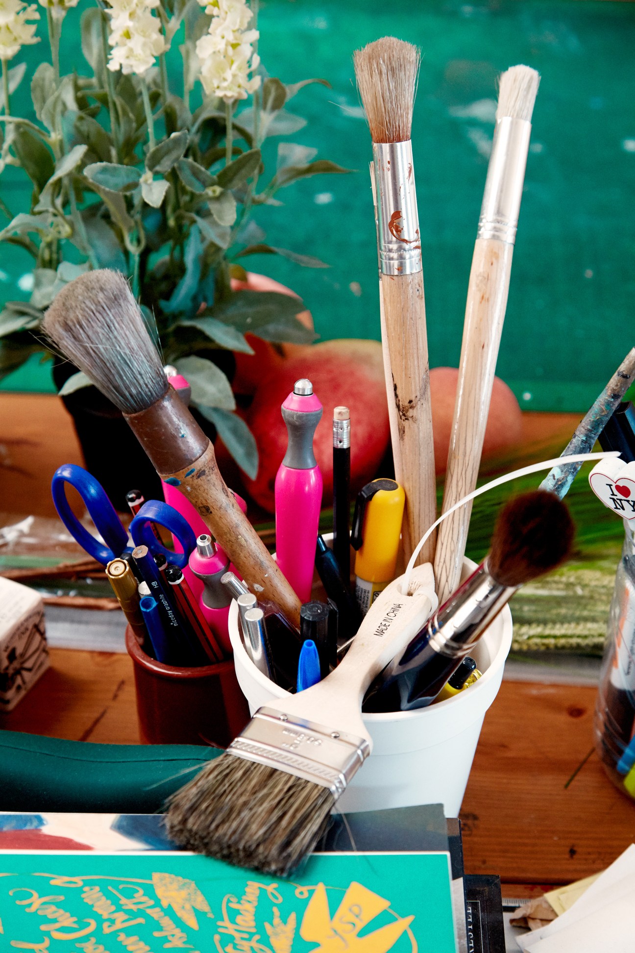 Artist's studio workspace with paintbrushes, markers, scissors and colored inks against a vibrant turquoise background.
