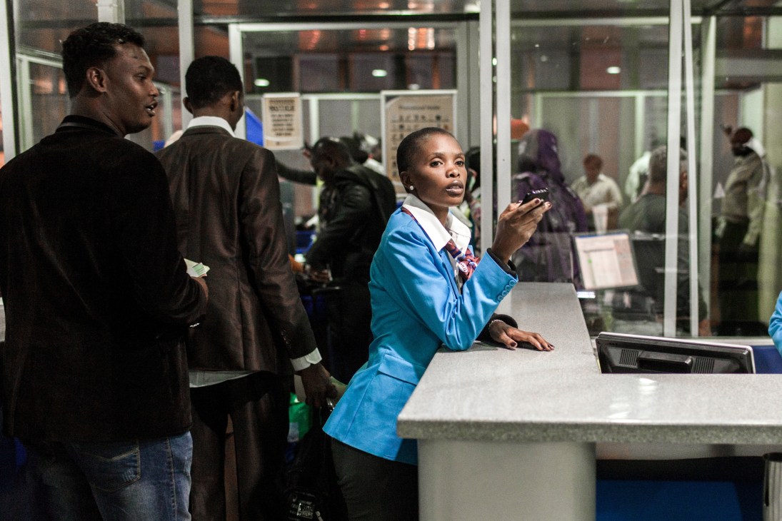 Woman in blue uniform at airport counter assisting passengers in Nairobi.