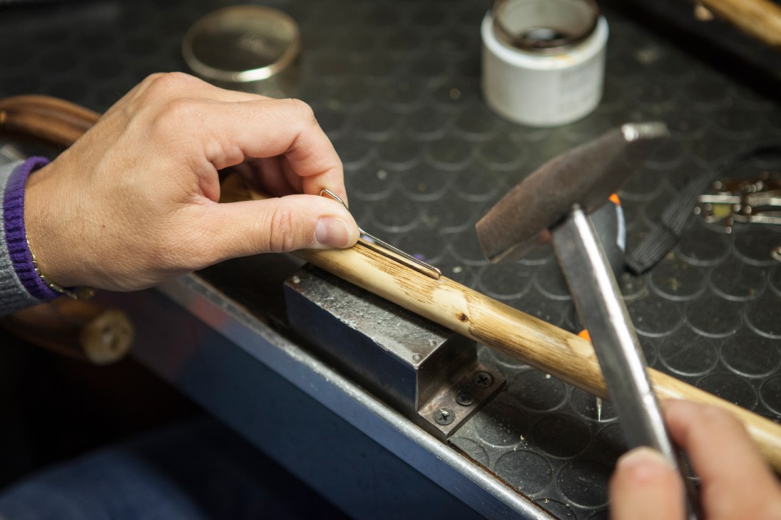 Craftsperson's hand inserting a metal spring onto a wooden umbrella shaft.