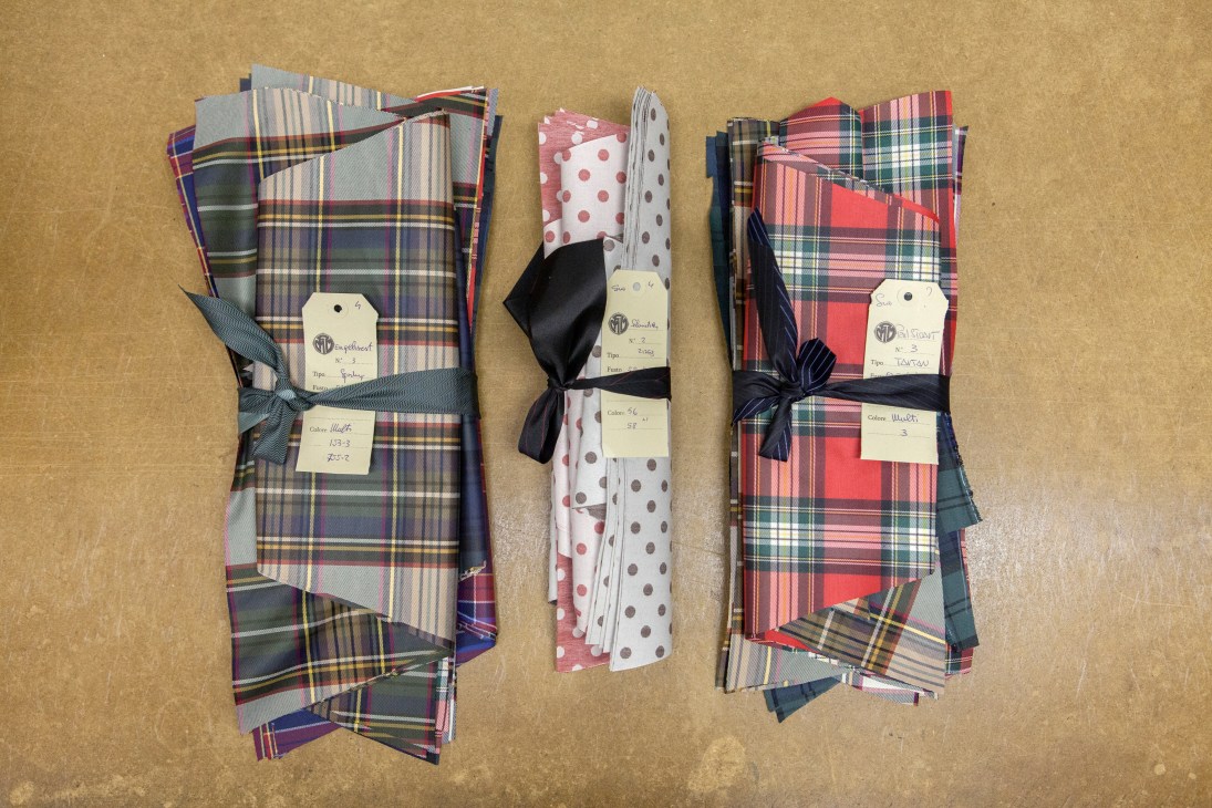 Three rolls of fabric with plaid and polka dot patterns tied with ribbons, displayed on a tan surface with product tags.