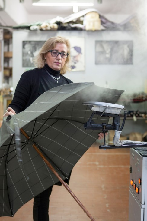Woman steaming an umbrella canopy to remove creases in a workshop.