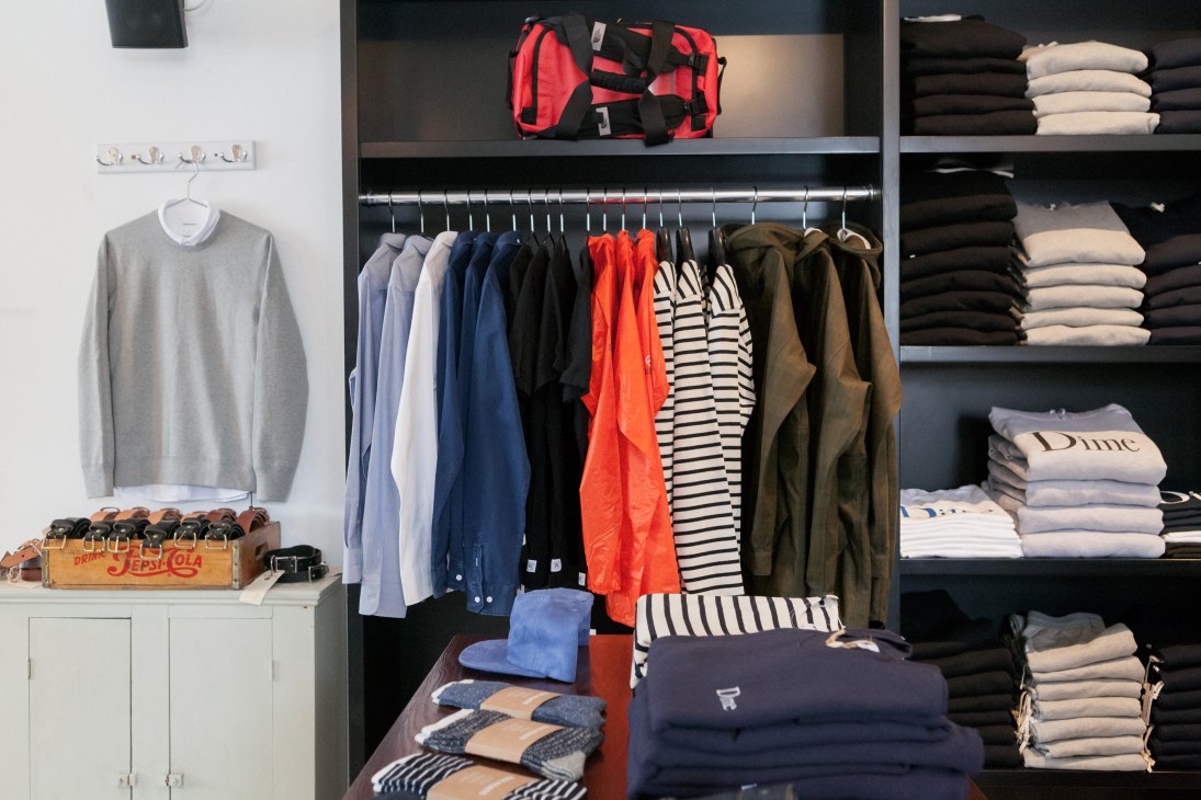 Interior of Savoie Fils store with organized display of clothing including sweaters, shirts and jackets on hangers and shelves.