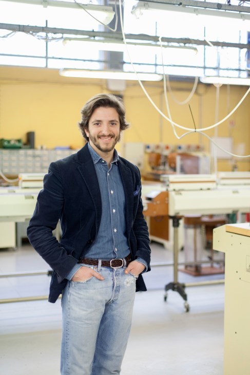 Adriano Meneghetti stands in his Milan workshop with hands in pockets, smiling at camera.