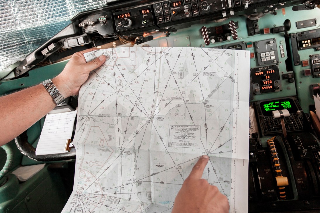 Pilot's hands holding a flight chart in an aircraft cockpit with instruments visible.